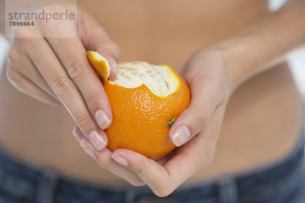 Nahaufnahme einer Frauenhand  die eine Orange schält.