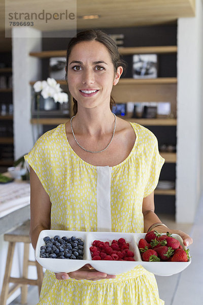 Porträt einer Frau  die zu Hause ein Tablett mit verschiedenen Beeren hält.