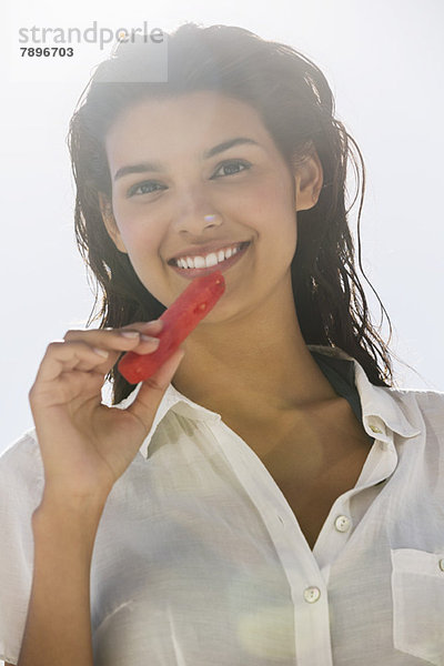 Schöne Frau  die eine Scheibe Wassermelone am Strand isst.