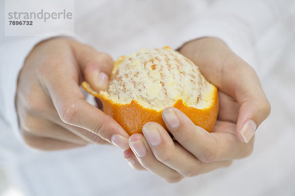 Nahaufnahme einer Frauenhand  die eine Orange schält.