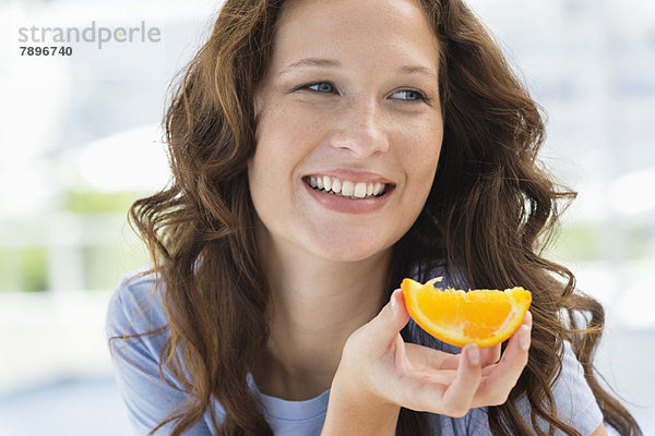 Nahaufnahme einer lächelnden Frau mit einer Orangenscheibe