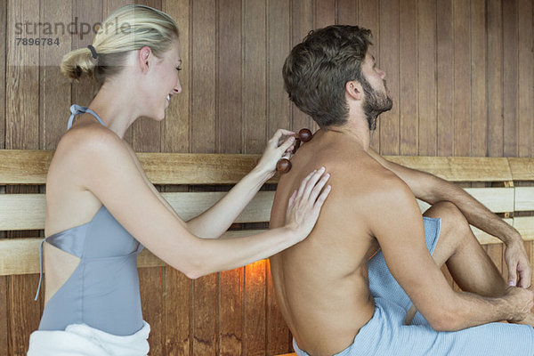 Frau massiert den Rücken ihrer Freundin mit einem Massagegerät in der Sauna.