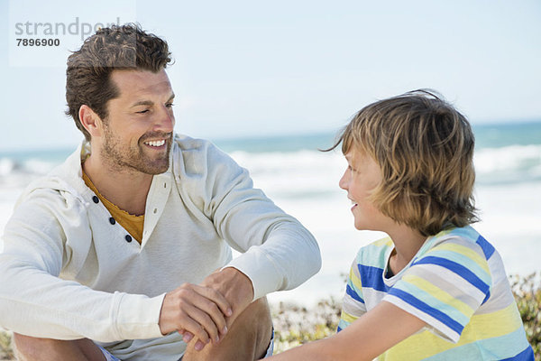 Mann sitzend mit seinem Sohn am Strand
