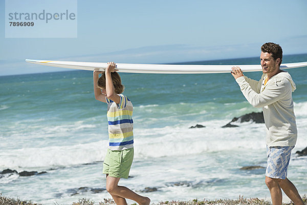 Mann und Sohn mit Surfbrett am Strand