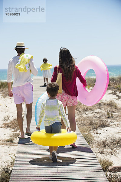 Kinder mit ihren Eltern halten aufblasbare Ringe an einer Strandpromenade.