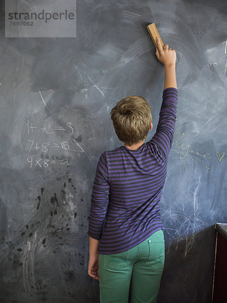 Junge putzt Tafel mit einem Staubwedel im Klassenzimmer