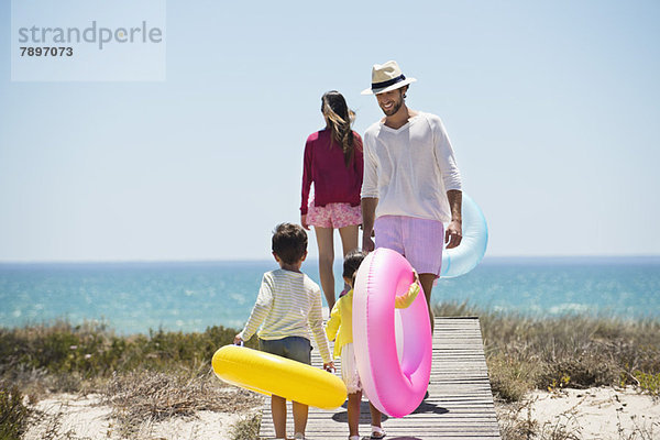 Kinder mit ihren Eltern halten aufblasbare Ringe an einer Strandpromenade.