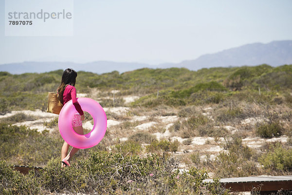 Frau hält einen aufblasbaren Ring und geht auf einer Strandpromenade spazieren.
