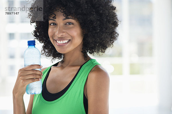 Lächelnde Frau trinkt Wasser aus einer Flasche