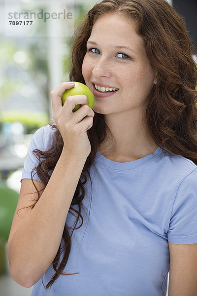 Frau isst einen grünen Apfel und lächelt