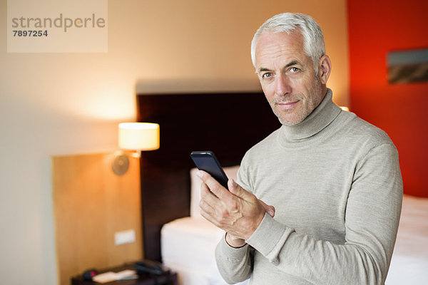 Ein Mann  der ein Handy in einem Hotelzimmer benutzt.