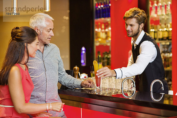 Barkeeper  der einem Paar an der Theke einen Drink serviert.
