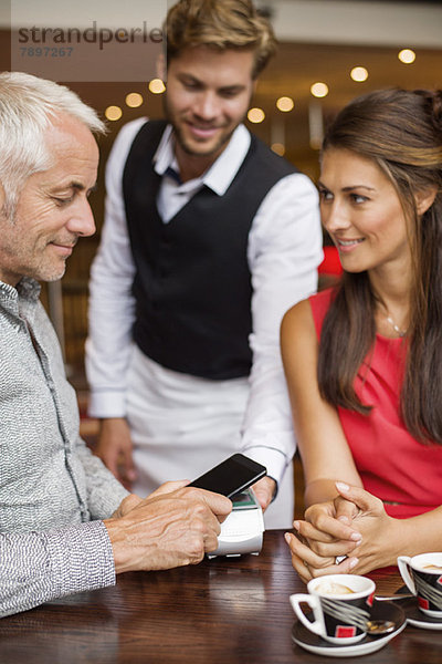 Kellner zeigt einem Paar auf einem Tisch in einem Restaurant ein Kreditkartenlesegerät.