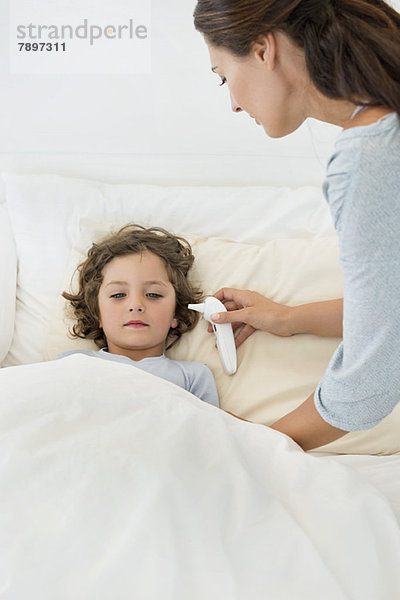 Frau überprüft Fieber ihres Sohnes mit einem Thermometer