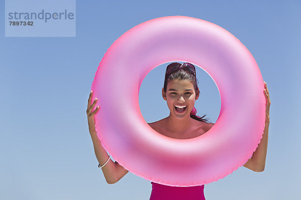 Schöne Frau  die durch einen aufblasbaren Ring am Strand schaut.