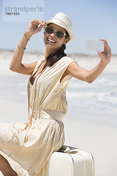 Schöne Frau  die ein Foto von sich selbst mit einem Handy am Strand macht.