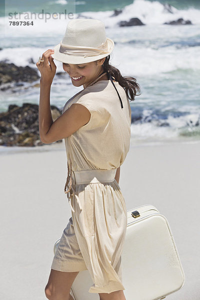 Schöne Frau mit Koffer am Strand