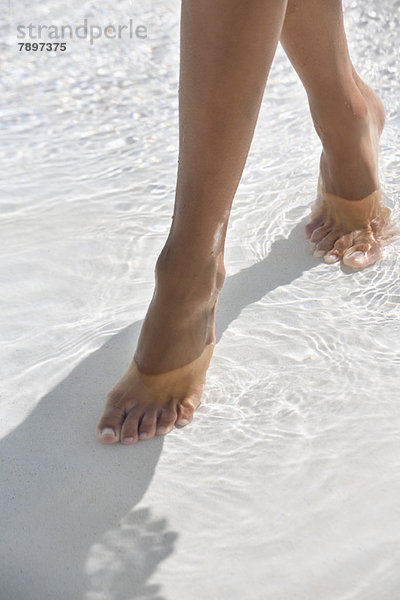 Frau  die im Wasser am Strand spazieren geht.