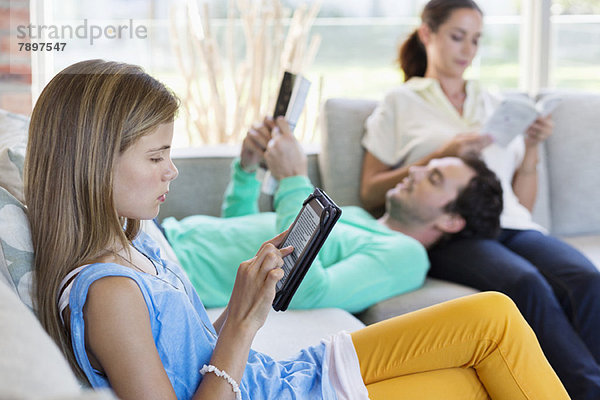 Mädchen  das ein digitales Tablett benutzt  während ihre Eltern zu Hause Bücher lesen.