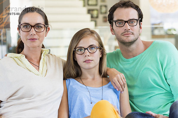 Porträt einer Familie  die auf einer Couch sitzt und eine Brille trägt.