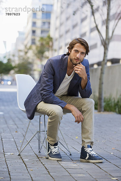 Porträt eines Mannes  der auf einem Stuhl auf einer Straße sitzt.