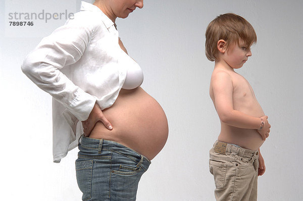 Schwangere Frau mit freiem Bauch steht neben Jungen mit nacktem Bauch
