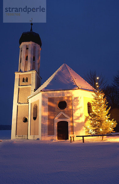 Beleuchtete Kapelle und Weihnachtsbaum in der Dämmerung im Winter