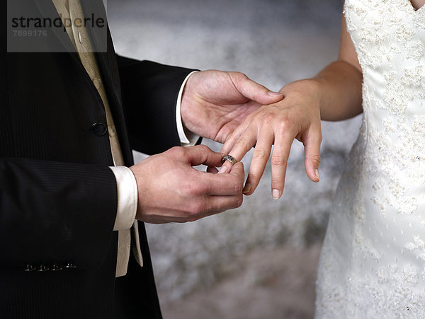 Brautpaar  Bräutigam steckt Braut Ring an den Finger