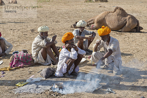 Vier ältere Inder mit Turban und dem traditionellen Beinkleid Dhoti hocken am Boden  auf einer Feuerstelle wird Essen zubereitet  Kamelmarkt
