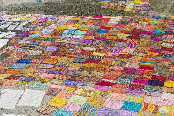 Bunte Saris sind nach dem Waschen zum Trocknen auf einer Sandbank am Flussufer des Yamuna ausgelegt