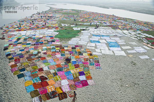 Bunte Saris sind nach dem Waschen zum Trocknen auf einer Sandbank am Flussufer des Yamuna ausgelegt
