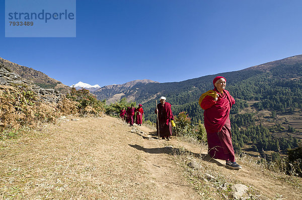 Mönche und Nonnen in roten Gewändern  zu Fuss auf einem Pfad an einem Berghang