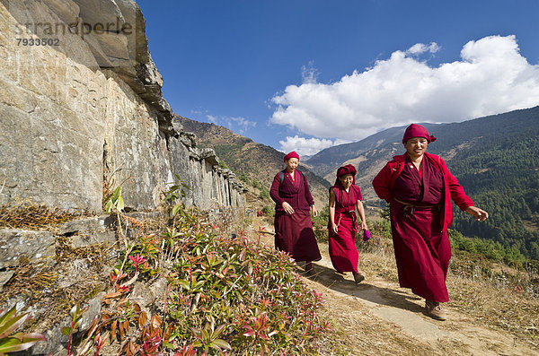 Mönche und Nonnen in roten Gewändern zu Fuß unterwegs auf einem Pfad an einem Berghang