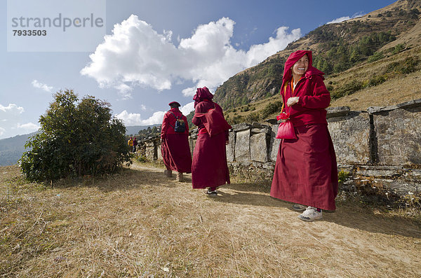 Mönche und Nonnen in roten Gewändern zu Fuß unterwegs auf einem Pfad an einem Berghang