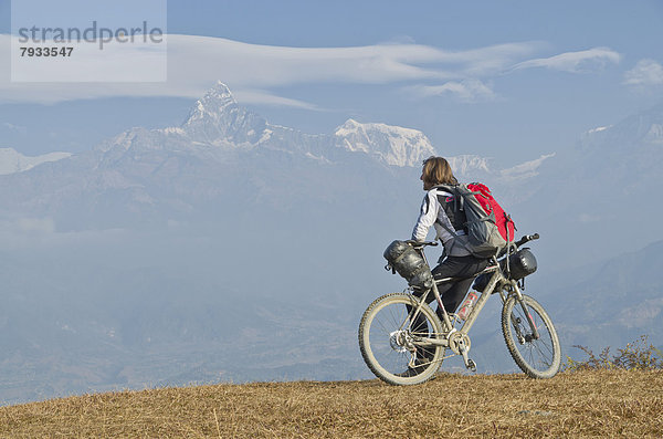 Ein Radfahrer stützt sich auf sein Fahrrad  mit Blick auf die Annapurna-Kette hinten