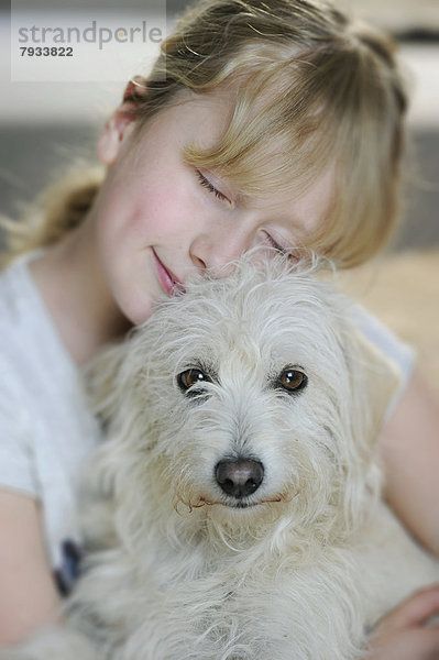 Mädchen  neun Jahre  schmust mit einem jungen Mischlingshund
