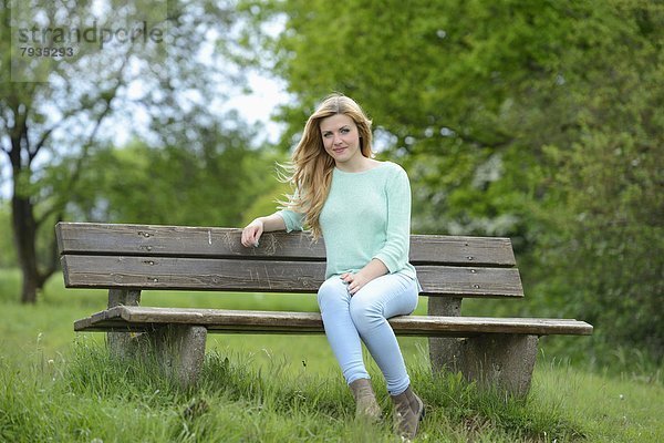 Blonde junge Frau sitzt auf einer Bank