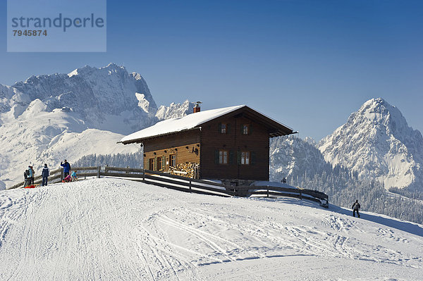 Holzhaus auf verschneitem Hügel  hinten die Alpspitze und Zugspitze