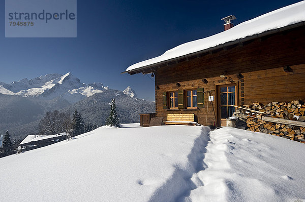 Holzhaus auf verschneitem Hügel  hinten die Alpspitze und Zugspitze