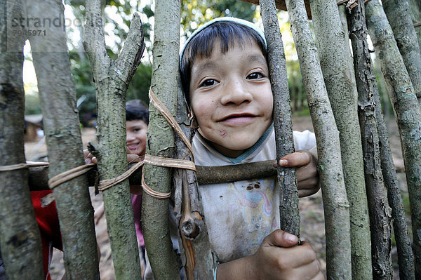 Frecher Junge  6 Jahre  schaut durch die Lücke in einem Zaun  in Gemeinde der Mbya-Guarani Indianer