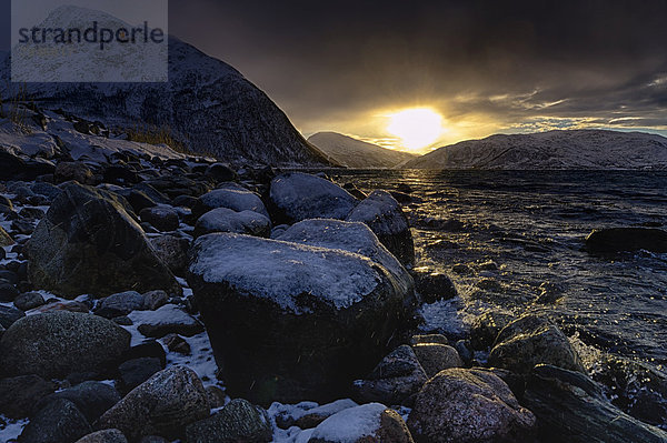Steine mit Schnee an Fjordufer bei Sonnenaufgang