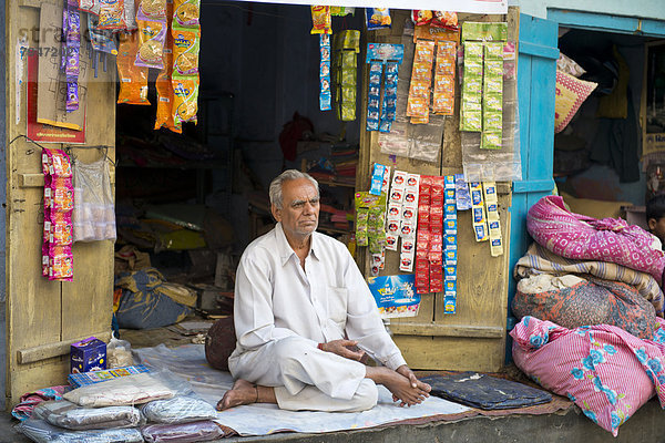 Älterer Inder sitzt auf einer Decke vor seinem Verkaufsstand