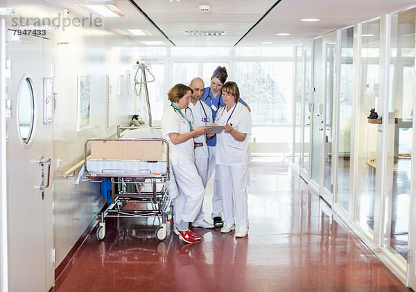 Volle Länge von vier Ärzten  die digitale Tabletten benutzen  während sie auf der Trage im Krankenhausflur stehen