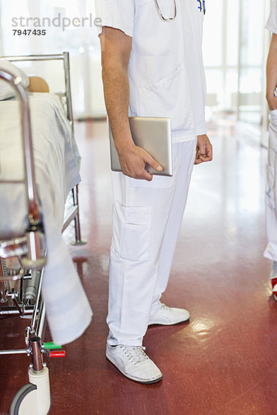 Niedriger Abschnitt des mittleren erwachsenen männlichen Arztes  der eine digitale Tablette hält  während er auf der Trage steht.