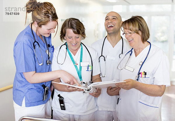 Glückliche Ärzte und Ärztinnen lachen beim Lesen von Ringbüchern im Krankenhaus