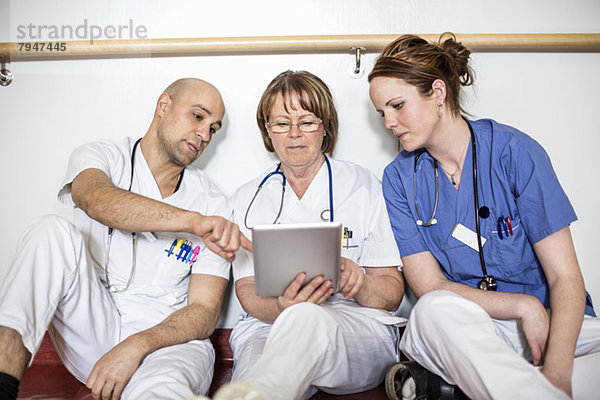 Ärzte mit digitalem Tablett beim Anlehnen an die Wand im Krankenhaus