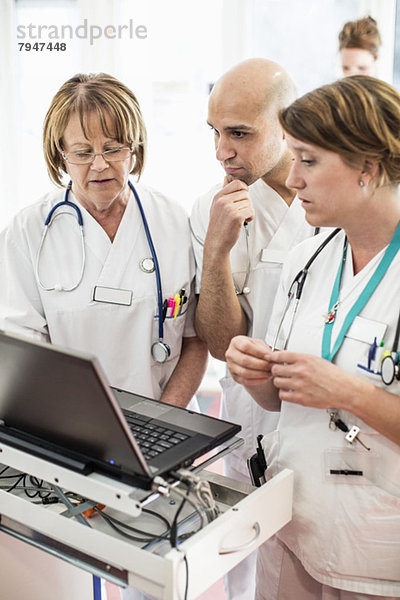 Arzt und Ärztin diskutieren über Laptop mit Kollegen im Krankenhaus