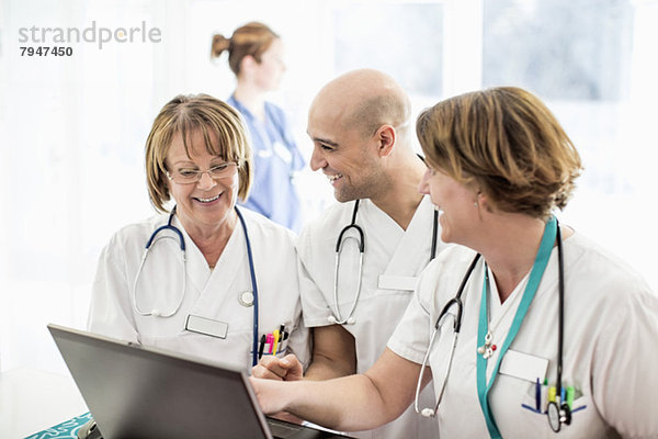 Glückliche Ärztinnen und Ärzte mit Laptop im Krankenhaus