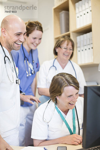 Glückliche Ärzte und Ärztinnen beim Blick auf den Computer am Schreibtisch im Krankenhaus