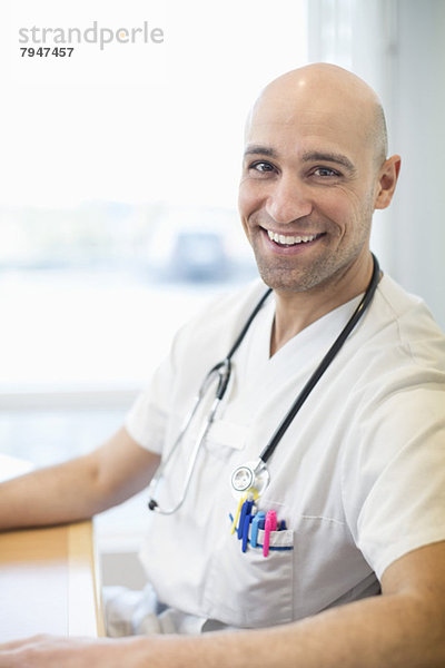 Porträt des glücklichen Arztes am Schreibtisch im Krankenhaus